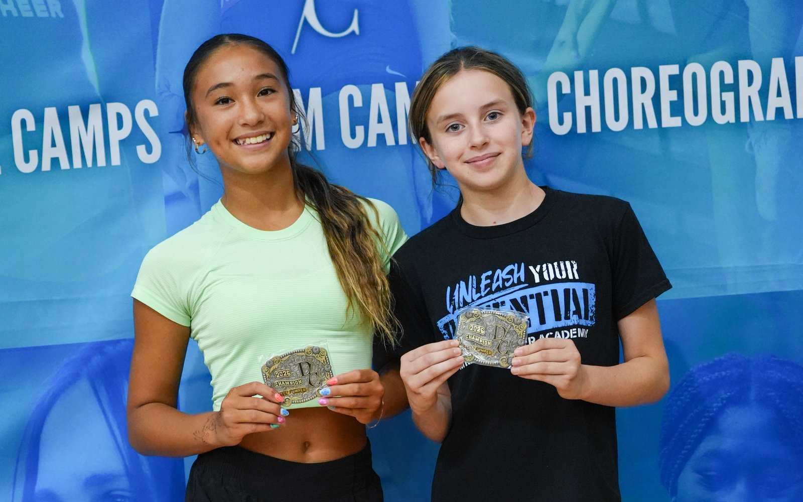 Two campers smiling and holding Dream Camps champion belt buckles